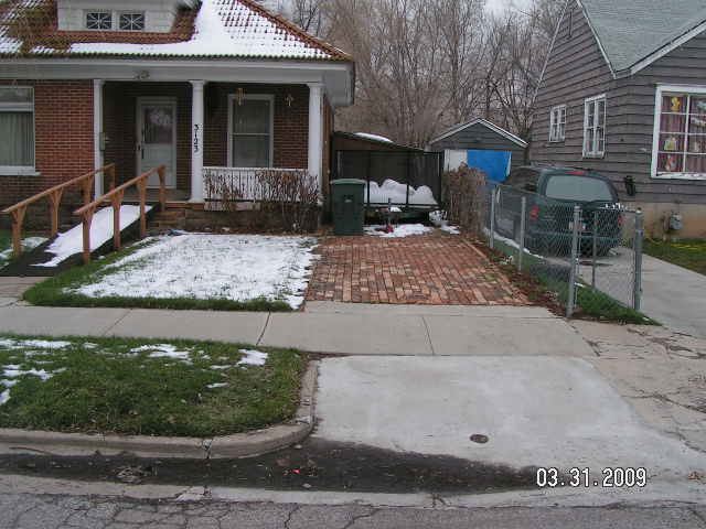 A red brick house with overgrown landscaping and a truck parked in front of it.